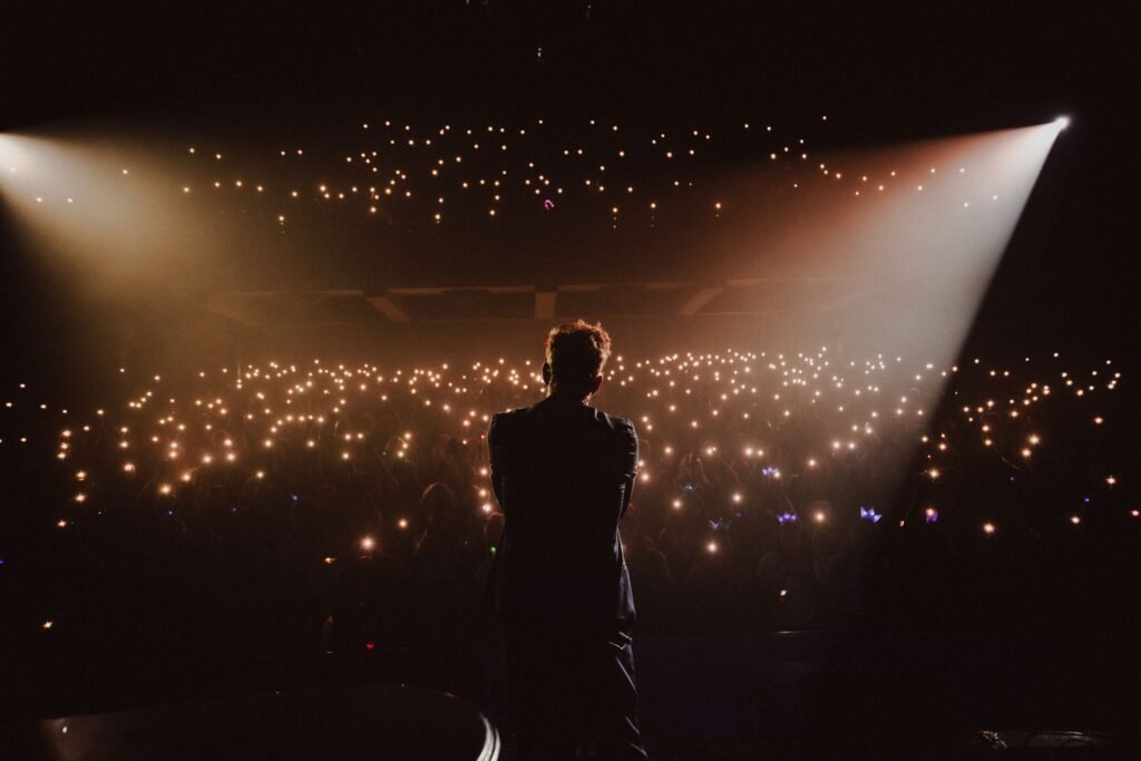 El cantante Axel de espaldas en el escenario, frente a un público multitudinario que ilumina la sala con las linternas de sus móviles durante un concierto.