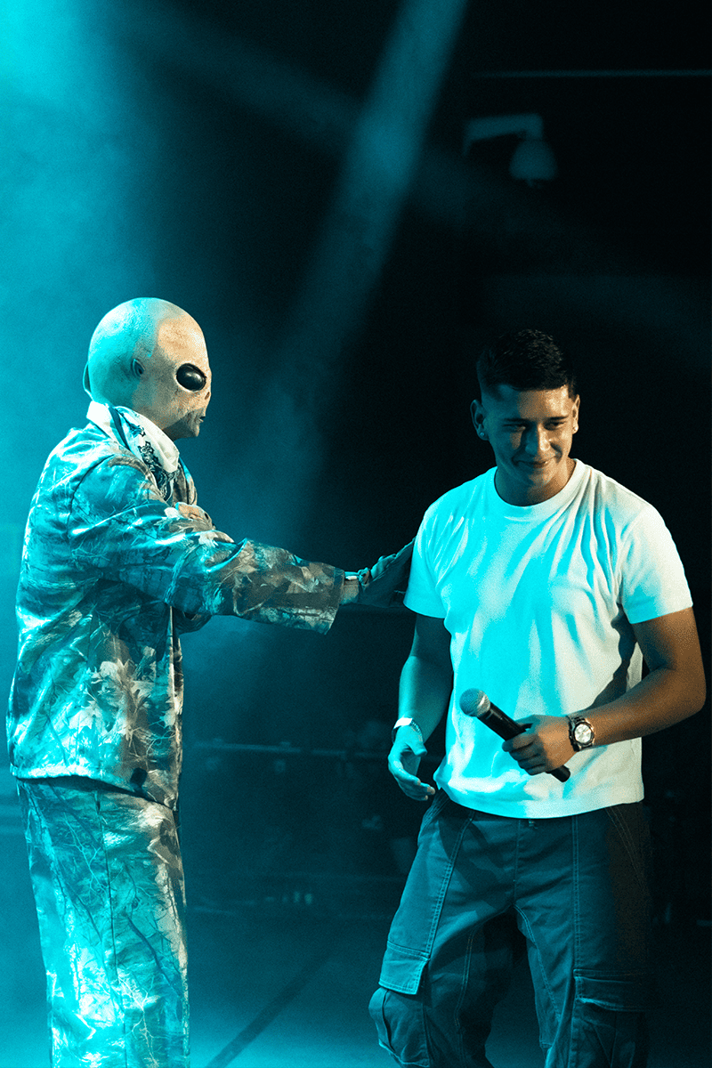El artista Nakku en el escenario junto a Mante, caracterizado con una máscara de alienígena, durante una actuación en directo.