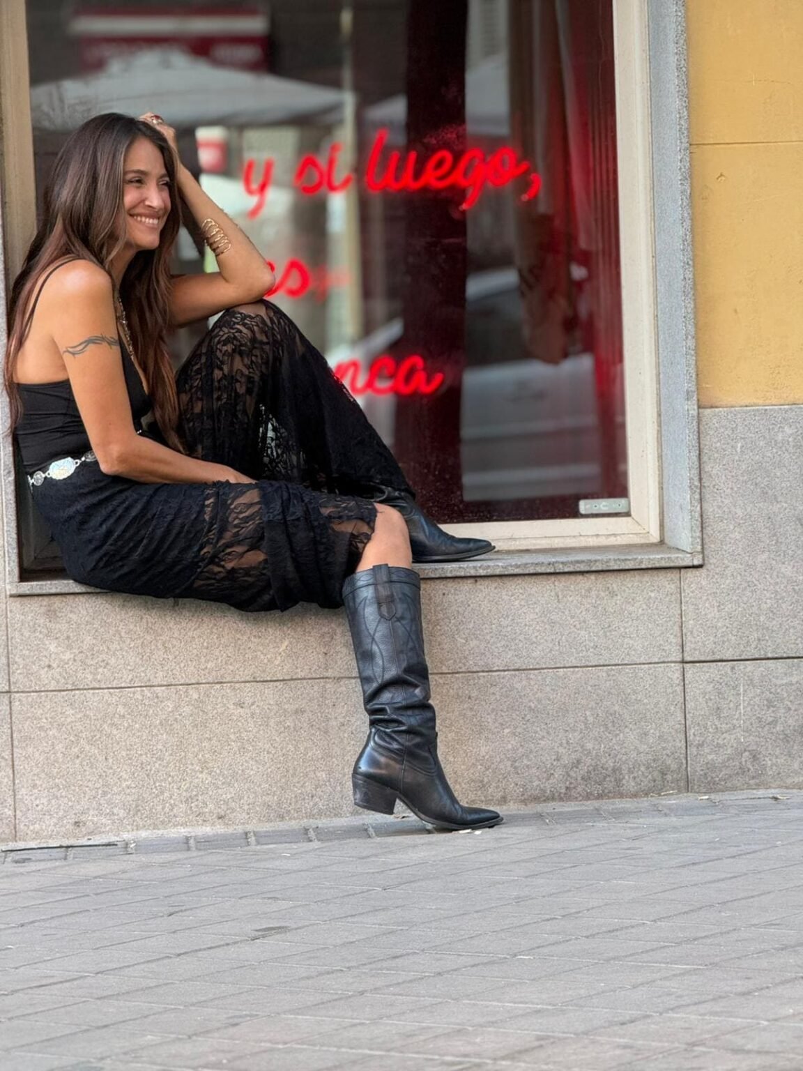La cantautora Georgina sentada en el alféizar de un escaparate, sonriendo junto a un neón rojo.