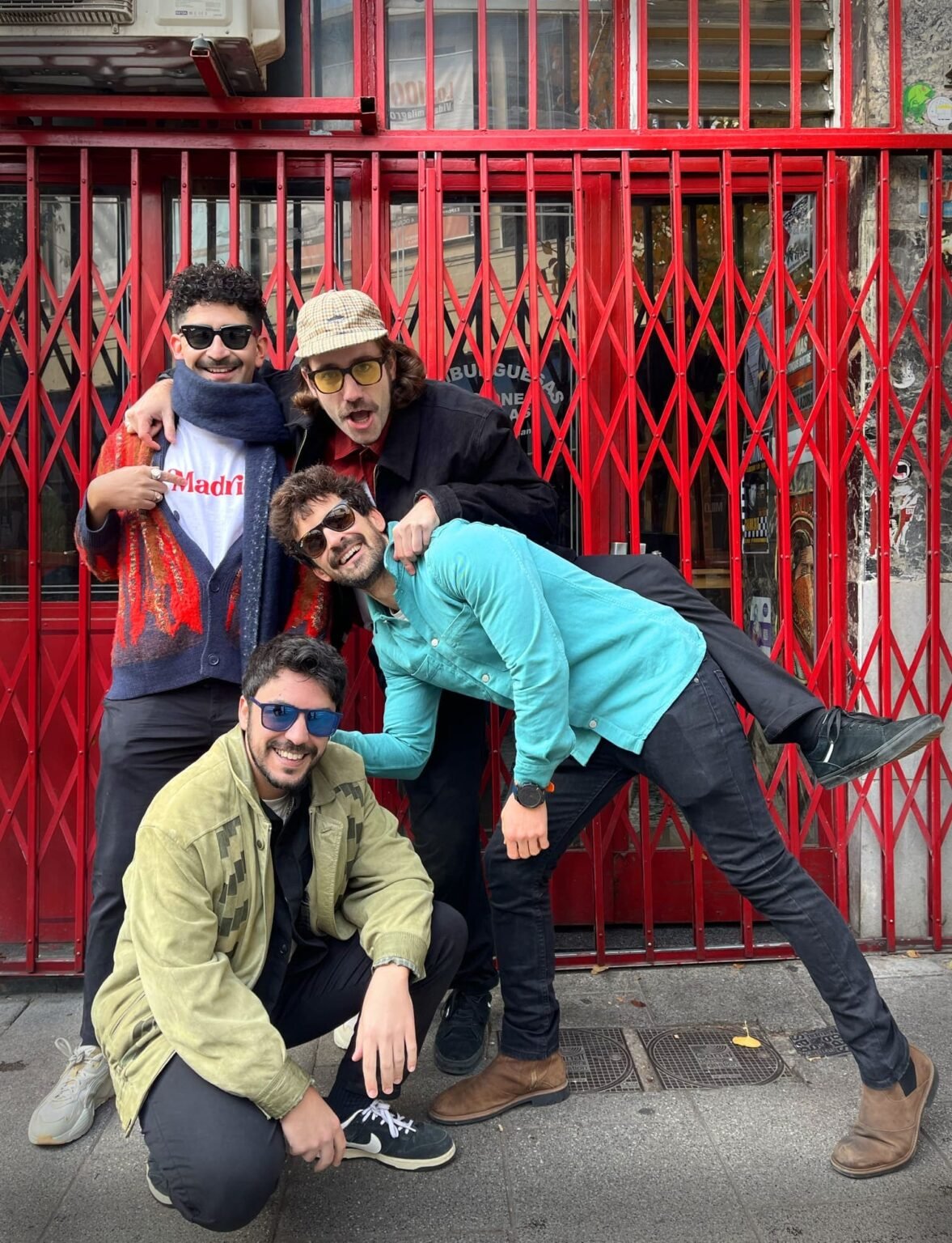 La banda CABO VENTURA posando de manera informal y divertida frente a una verja roja en la calle.